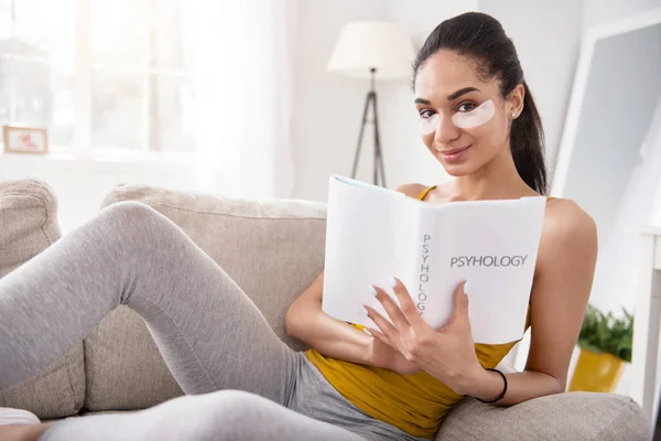 Charming woman posing with psychology book on couch