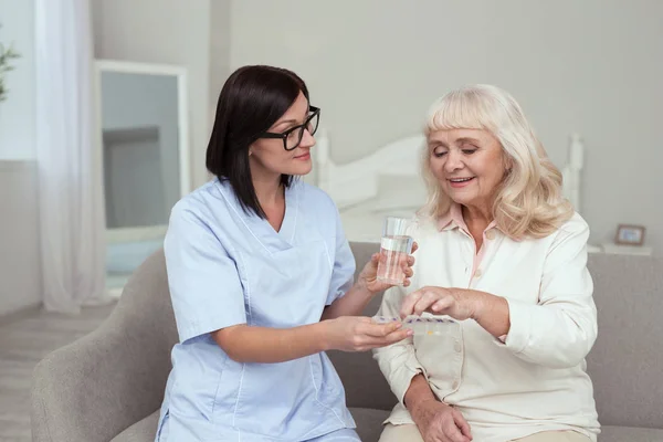 Чарівна медсестра дає таблетки літній жінці — стокове фото