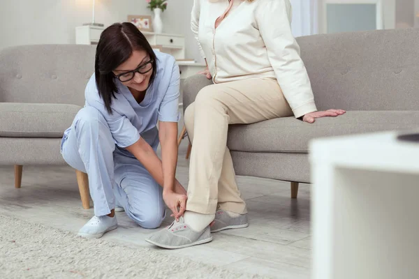 Giovane infermiera portando pantofole alla donna anziana — Foto Stock