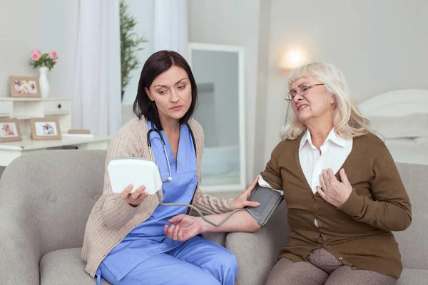Preocupado cuidador feminino controlando a pressão arterial — Fotografia de Stock