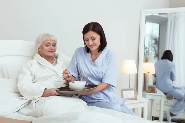 Cuidador positivo dando comida a la anciana — Foto de Stock