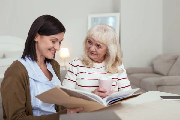 Happy elder woman and caregiver watching photo album — Stock Photo, Image