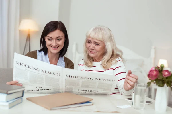 Mulher idosa ativa e cuidador ler jornal — Fotografia de Stock