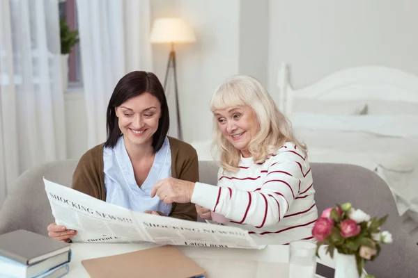 Mujer anciana inspirada y cuidador examinando periódico — Foto de Stock