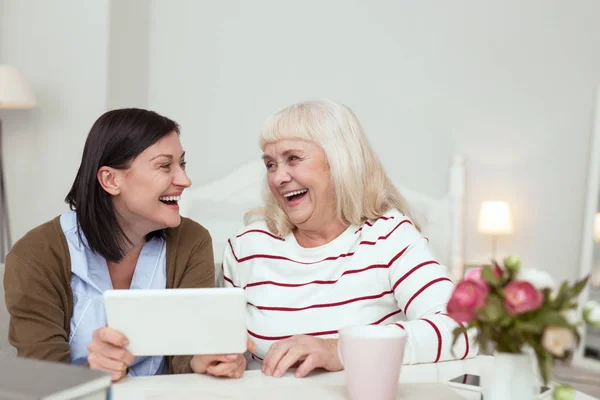 Cheerful elder woman and caregiver playing on tablet