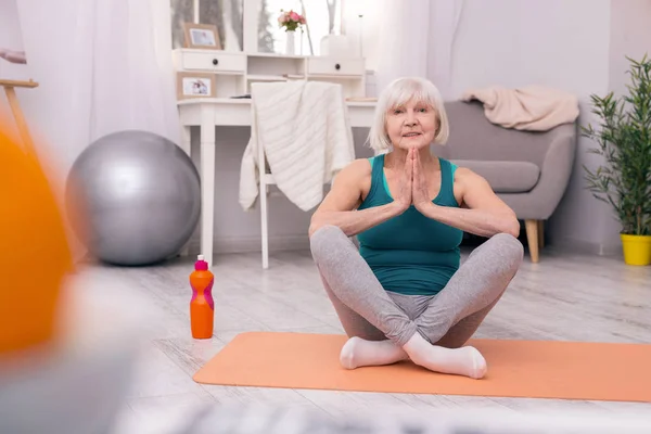 Charming elderly woman meditating at home