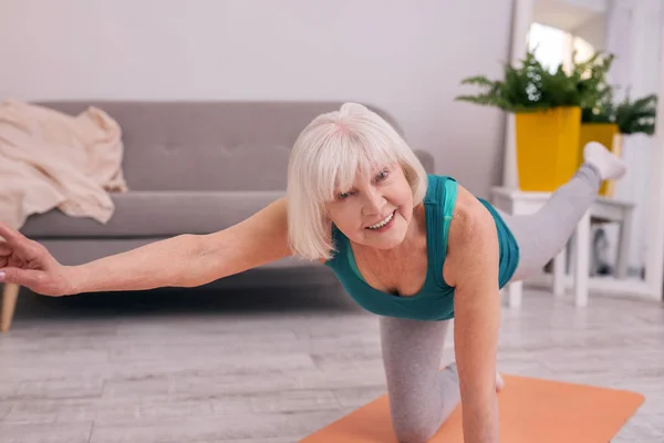 Optimistische ältere Frau beim Dehnen, während sie auf einem Knie steht — Stockfoto