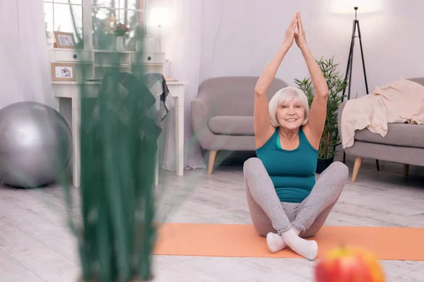 Gai femme âgée souriant joyeusement tout en pratiquant le yoga — Photo