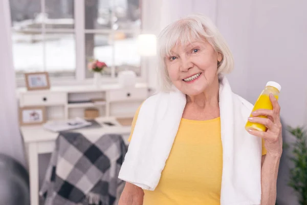 Счастливая пожилая женщина позирует с бутылкой сока после тренировки — стоковое фото