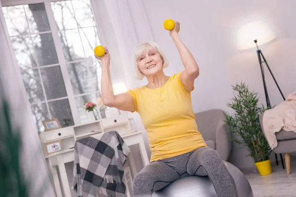 Donna anziana sorridente ed esercizio con manubri sulla palla yoga — Foto Stock