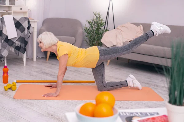 Atlética anciana estirándose sobre esterilla de yoga —  Fotos de Stock