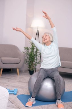 Neşeli kadın kıdemli yoga topu üzerinde otururken yana doğru eğilerek