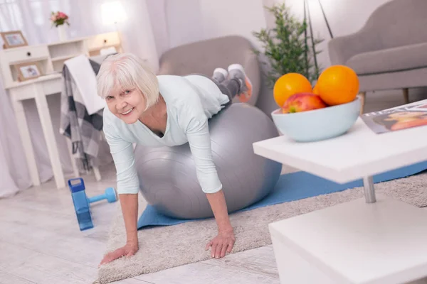 Очаровательная старшая женщина делает доску, лежа на мяче для йоги — стоковое фото