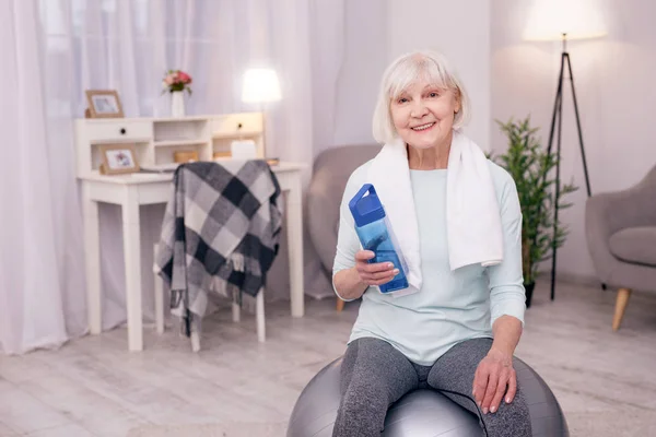 Idős asszony ül a jóga labdát, és a gazdaság a vizes palackot — Stock Fotó