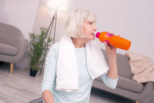 Pleasant senior woman drinking water after a workout
