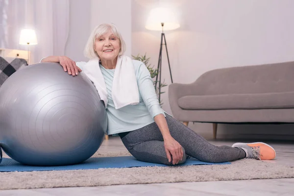 Cheerful elderly lady posing while leaning on yoga ball