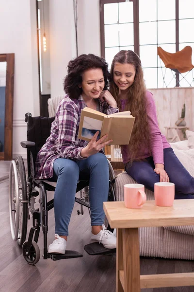 Оптимистичная женщина-инвалид и девушка читают вместе — стоковое фото