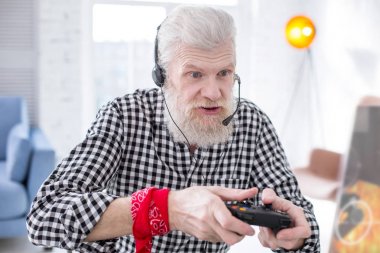 Bearded senior man being immersed into playing video game clipart