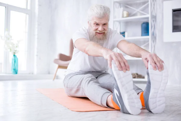 Upbeat elderly man stretching and touching his toes — Stock Photo, Image