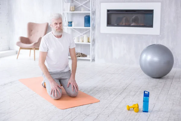 Hombre mayor de pelo blanco arrodillado en esterilla de yoga —  Fotos de Stock