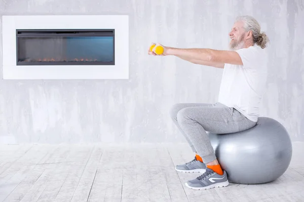 Elderly man sitting on fitness ball and exercising with dumbbells