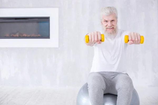 Очаровательный пожилой человек держит гантели, сидя на фитнес-мяч — стоковое фото