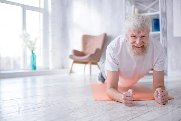Веселый пожилой человек делает упражнения на доске — стоковое фото