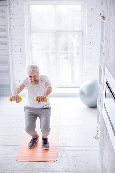 Agradable anciano haciendo sentadillas y sosteniendo mancuernas —  Fotos de Stock