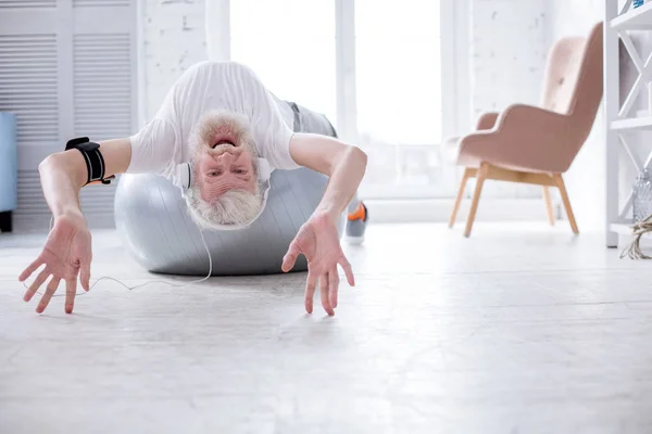 Hombre mayor alegre acostado en la bola de yoga y escuchando música —  Fotos de Stock