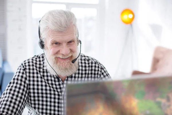 Joyful senior man smiling while playing game online