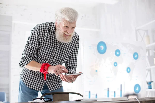 Pleasant senior man searching data from charts via phone — Stock Photo, Image