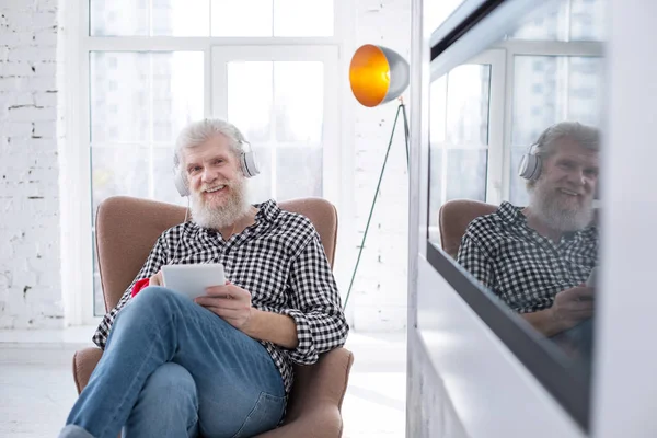 Agradável homem sênior sorrindo enquanto assiste filme no tablet — Fotografia de Stock