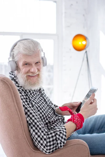 Upbeat senior man grinning while listening music in headphones