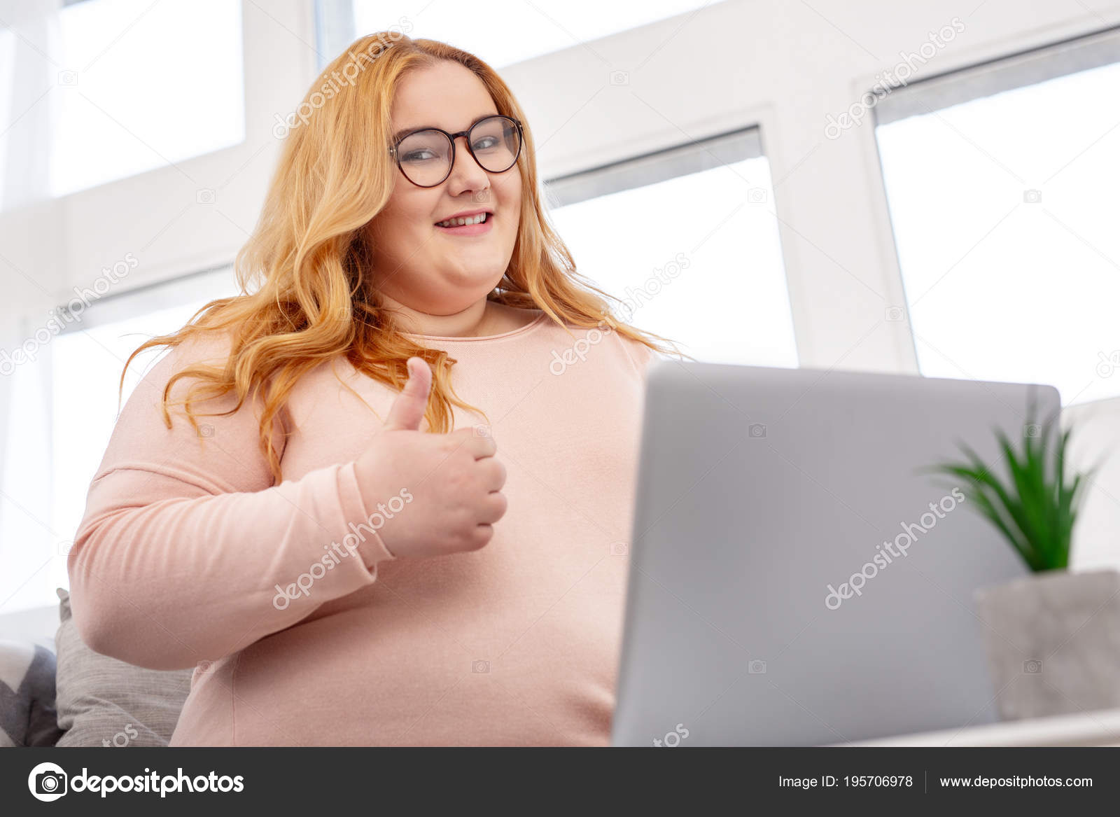 Cheerful plump woman showing her thumb up while working on her laptop - Sto...
