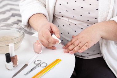 Overweight woman applying nude nail polish clipart