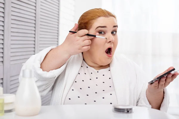 Концентрированная толстая женщина наносит макияж — стоковое фото