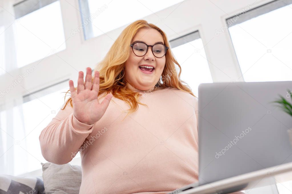 Happy fat woman waving and sitting with her laptop
