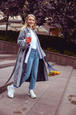 Elinde plastik bir bardak meyve suyuyla duran kız.