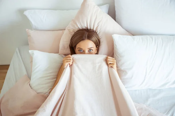 Cheerful brunette girl hiding her face under blanket — Stok fotoğraf