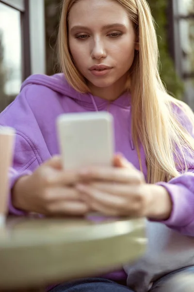 Сконцентрированная длинноволосая блондинка, пялящаяся на свой смартфон — стоковое фото