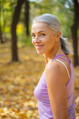 Gülümseyen güzel, beyaz, olgun bir bayan dışarıda dikiliyor.