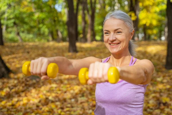 Glimlachende vrouw pompt haar biceps buiten — Stockfoto