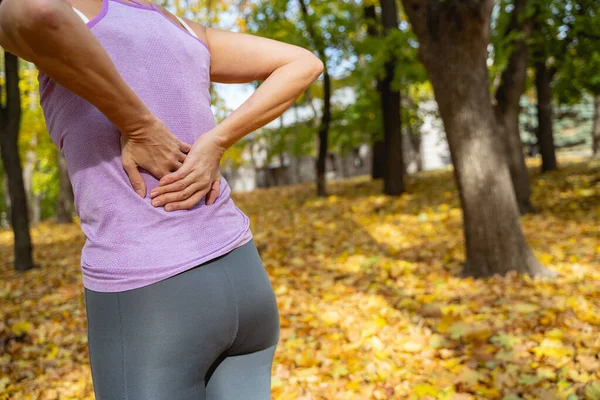 Hvit kvinne som berører sitt sår på ryggen utendørs – stockfoto