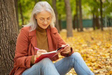 Gözlüklü gülümseyen bayan parkta yazıyor.