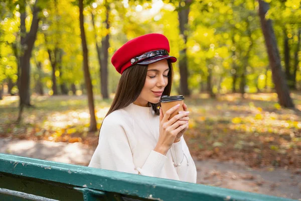 Veselá mladá žena těší chutné kávy v parku — Stock fotografie