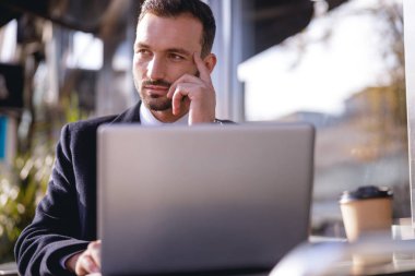 Laptopunun önünde oturan düşünceli sakallı adam.