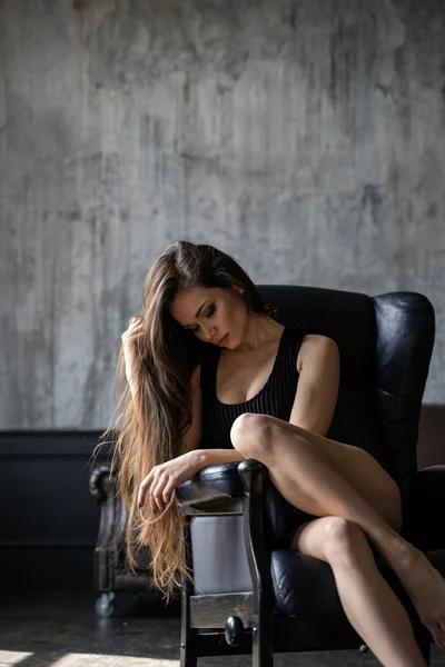 Femme avec des jambes fines sur chaise en cuir regardant vers le bas — Photo