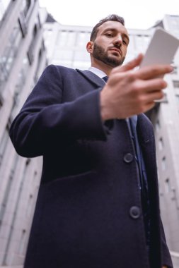 Konsantre olmuş esmer erkek, akıllı telefonuna bakıyor.