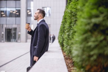 İş merkezinin yanında duran mutlu sakallı erkek.