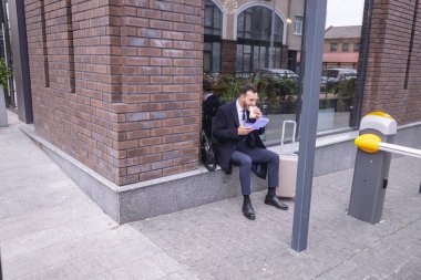 Aç sakallı ofis çalışanı sandviçini ısırıyor.